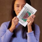 Woman holding the Expression Mandalas Coloring Book with mandala flower design on the cover