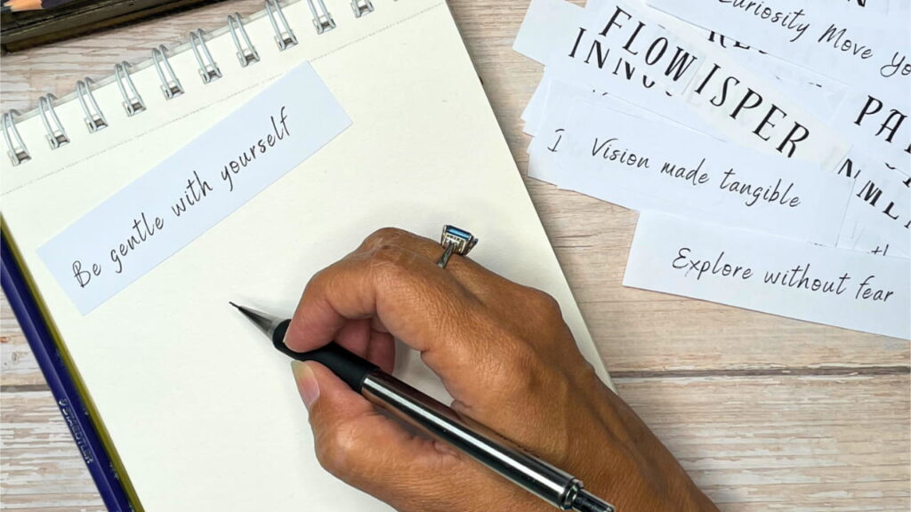 Hand writing in an art journal with archetype phrase cards nearby