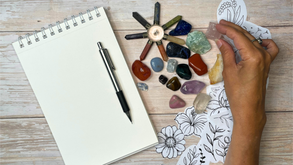 Hand holding an archetype crystal near an open art journal with stones and botanicals