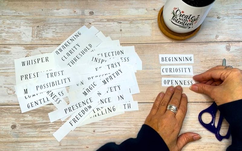 Hands selecting and aligning three cut paper words during a mindful creative process on a wooden table